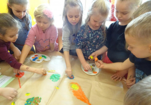 Ośmioro dzieci stempluje pomponami maczanymi w farbie sylwetę motyla.